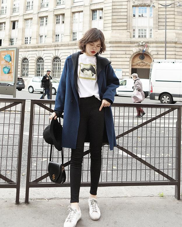 Cô gái diện áo khoác dạ dáng dài màu be, áo len trắng, quần skinny jeans và giày thể thao trắng