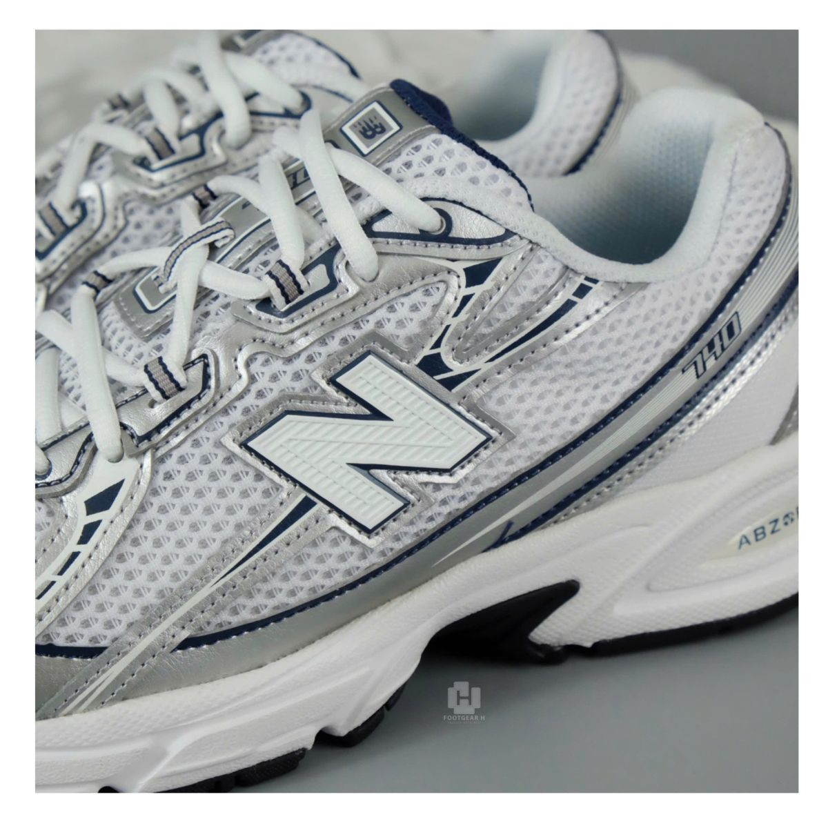 Đôi giày New Balance 740 màu bạc trắng với thiết kế cổ điển trên nền gỗ