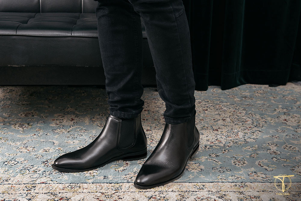 Người đàn ông mặc quần tây và áo sơ mi đứng với đôi Chelsea Boot màu nâu sẫm chụp kỷ yếu