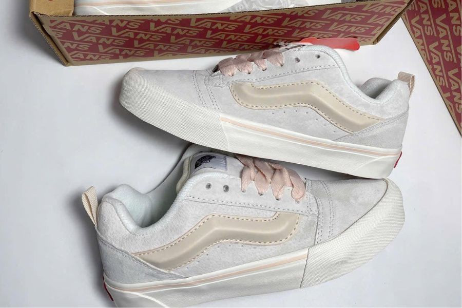 Nhiều đôi giày sneaker được trưng bày trên kệ gỗ trong một cửa hàng, với ánh sáng ấm cúng, tạo không gian mua sắm thân thiện cho những người yêu giày